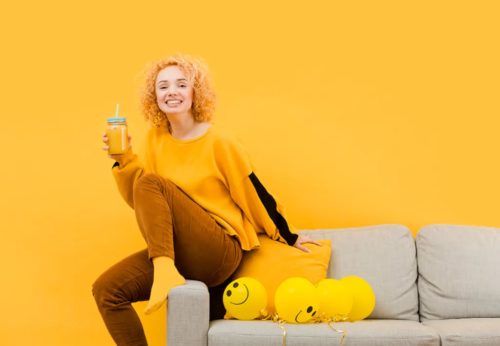 אשה שותה מיץ תפוזים נשענת על ספה בלוני סמיילי לידה
