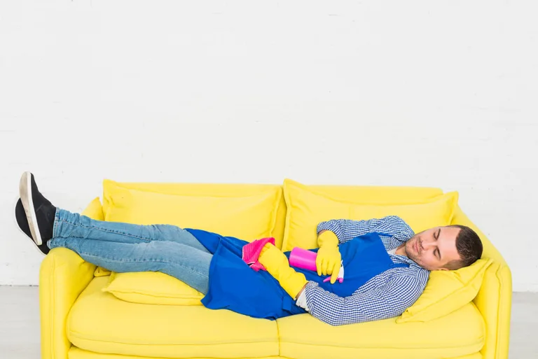 גבר עם סינר וכפפות ניקוי שוכב עייף על ספה צהובה