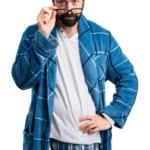 גבר מזוקן לבוש חלוק משובץ כחול מטה את המשקפיים במבט תוהה